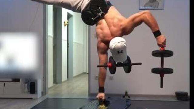 Man Performs One Arm Handstand On Bosu Ball While Holding Dumbbells With His Teeth